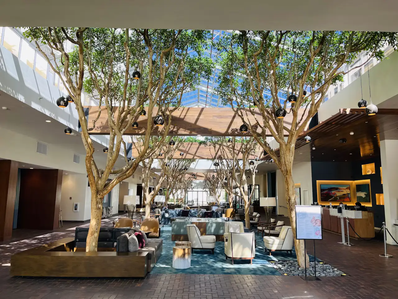 A hotel atrium lobby planted with mature trees beneath a glazed roof
